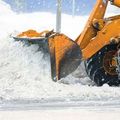 Orange snowplow blade pushing snow on a snowy road