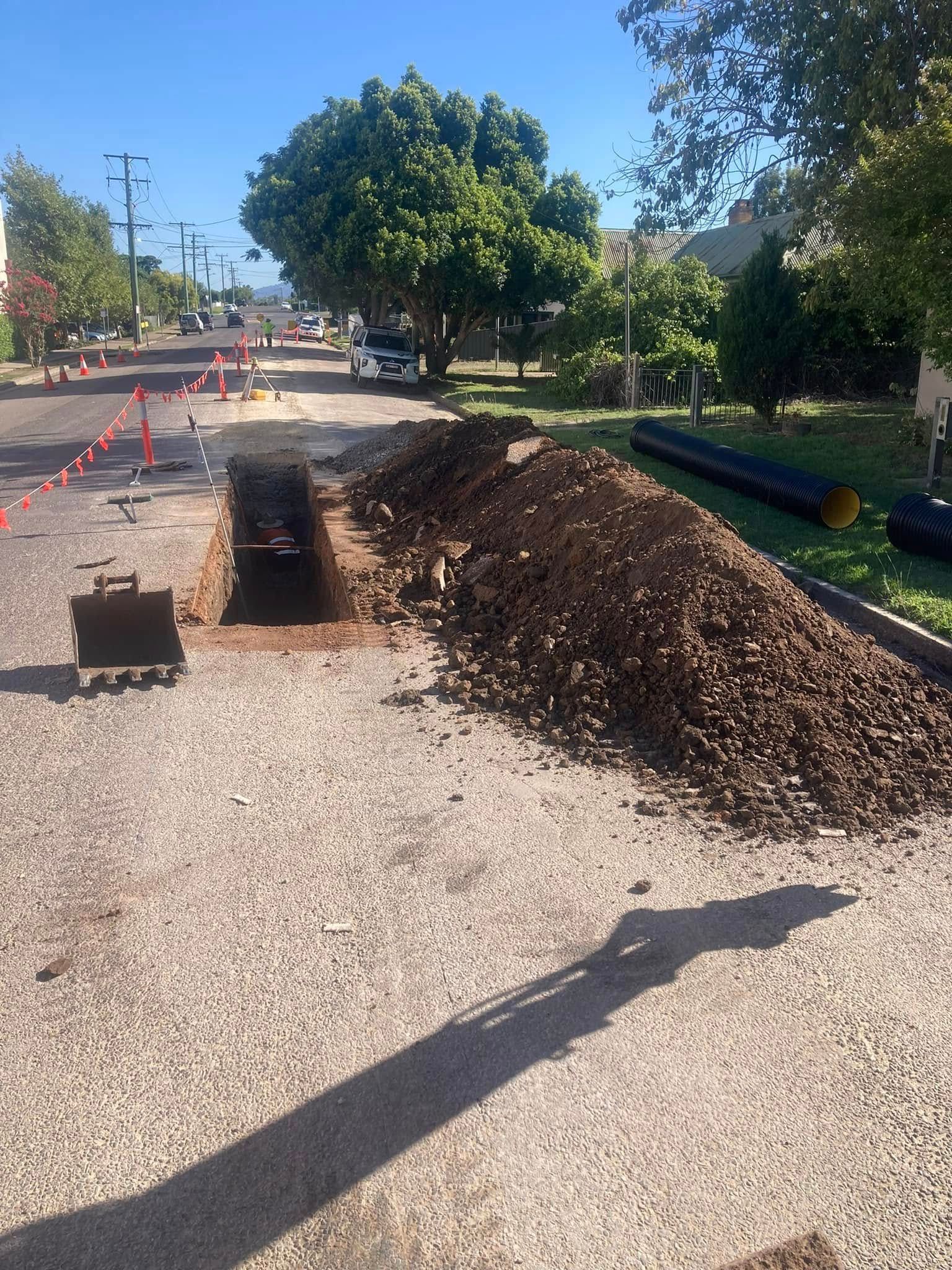 Roadwork trench beside a gravel path, with piles of soil and orange cones under a sunny sky. Roadwork trench beside a gravel path, with piles of soil and orange cones under a sunny sky.