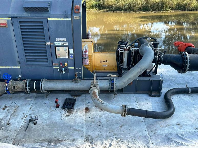 Industrial generator with black hoses and engine components on a concrete surface, partially covered in snow. Industrial generator with black hoses and engine components on a concrete surface, partially covered in snow.