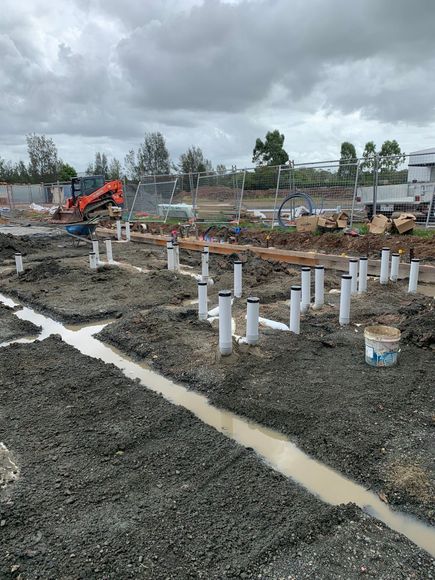 Construction site with gravel, white pipes, muddy trenches, and an excavator under cloudy skies Construction site with gravel, white pipes, muddy trenches, and an excavator under cloudy skies