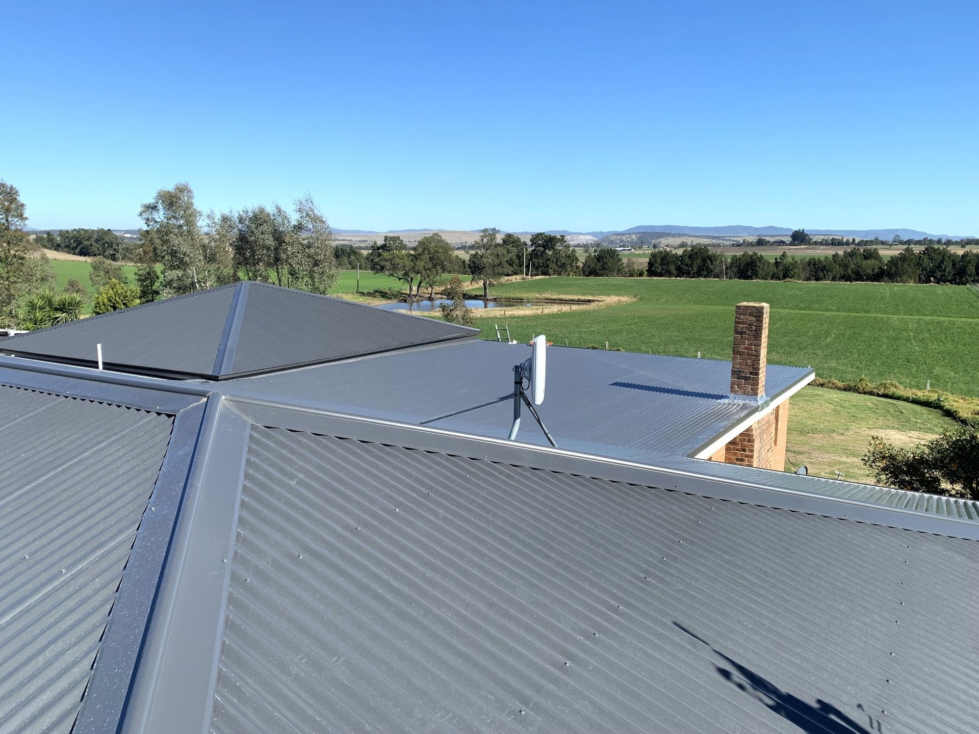 Solar roof panels with vent pipe overlooking green fields under a clear blue sky Solar roof panels with vent pipe overlooking green fields under a clear blue sky