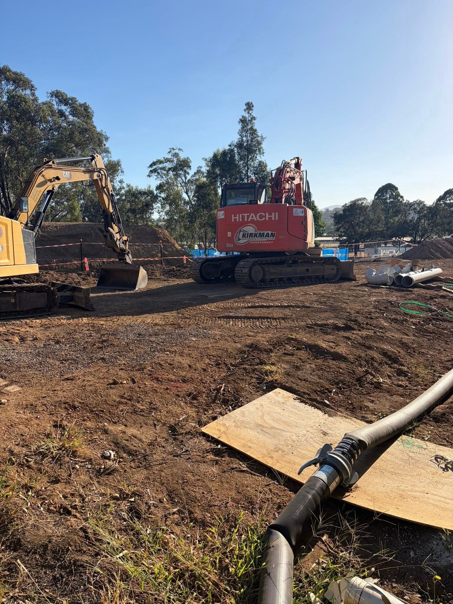 Excavator and red dump truck working on a dirt construction site under a clear blue sky Excavator and red dump truck working on a dirt construction site under a clear blue sky