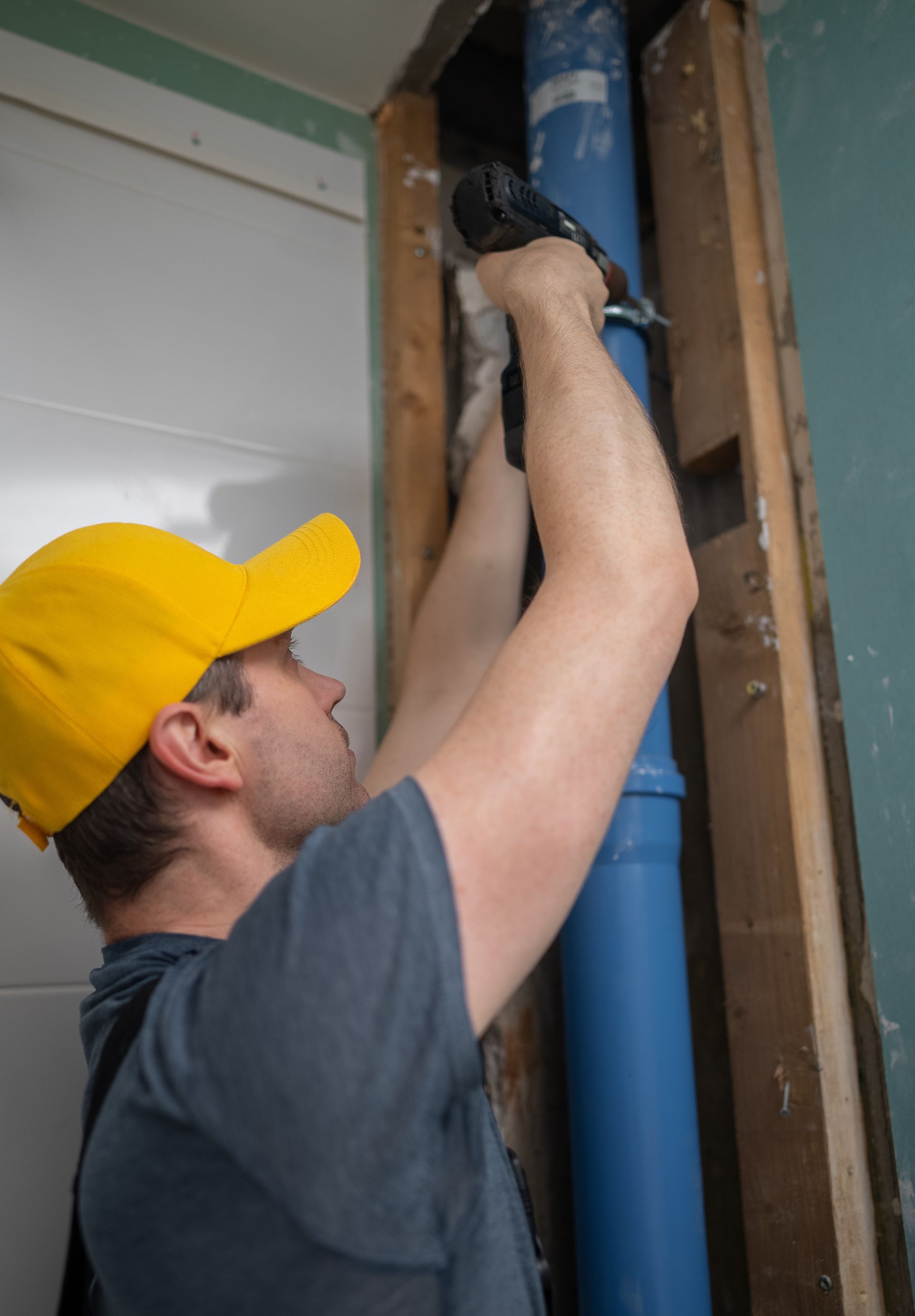 Technician in yellow cap adjusting blue pipes inside a wall cavity Technician in yellow cap adjusting blue pipes inside a wall cavity
