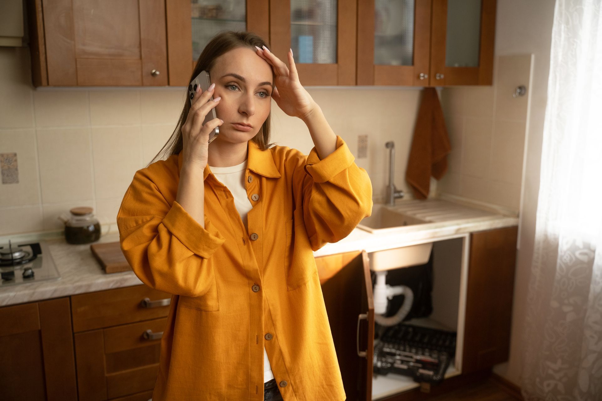 Person in a mustard yellow shirt on the phone in a kitchen, holding their head with a concerned expression Person in a mustard yellow shirt on the phone in a kitchen, holding their head with a concerned expression