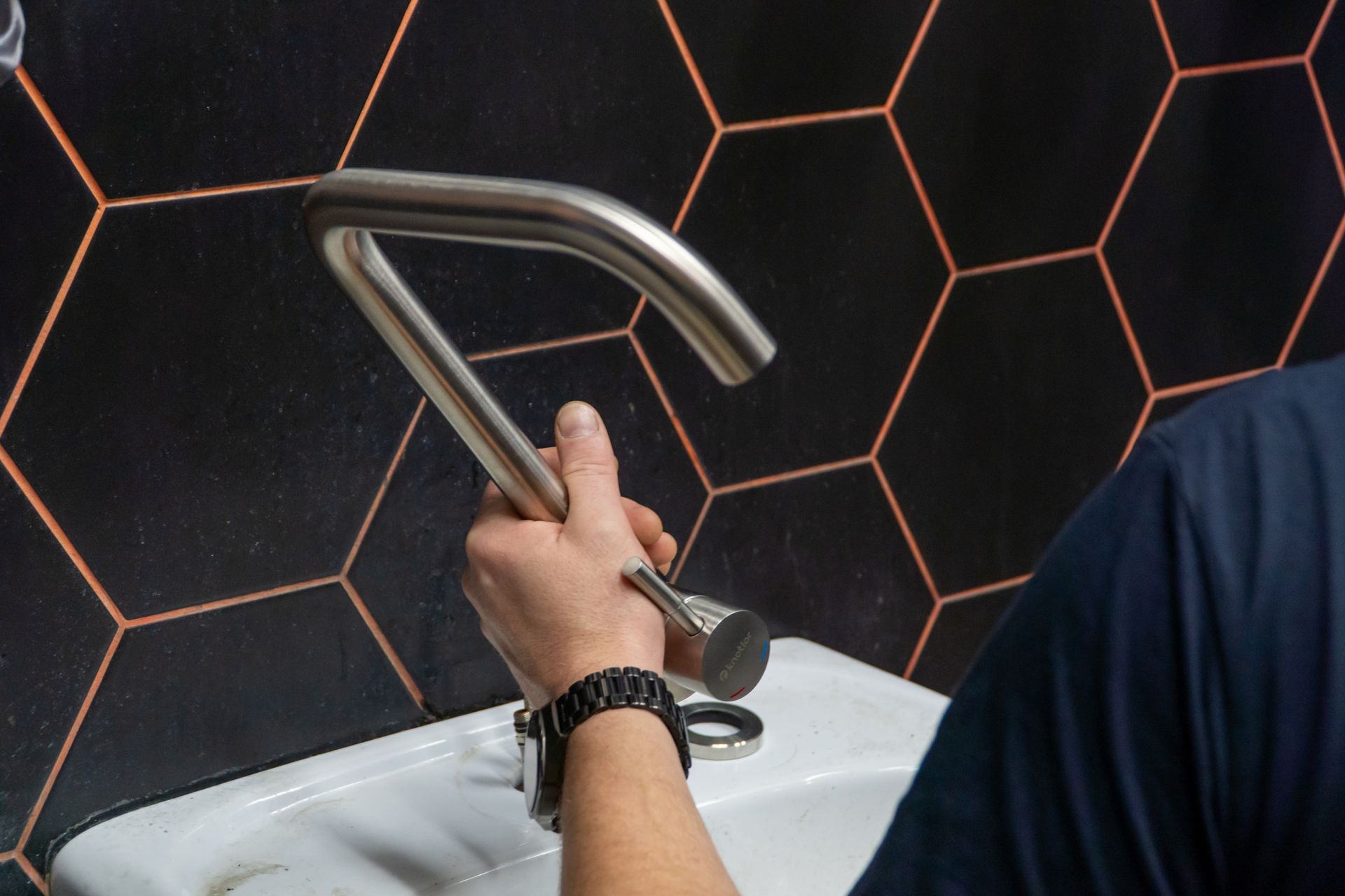 Hand washing at a white sink with a chrome faucet against a black hexagonal tile wall Hand washing at a white sink with a chrome faucet against a black hexagonal tile wall