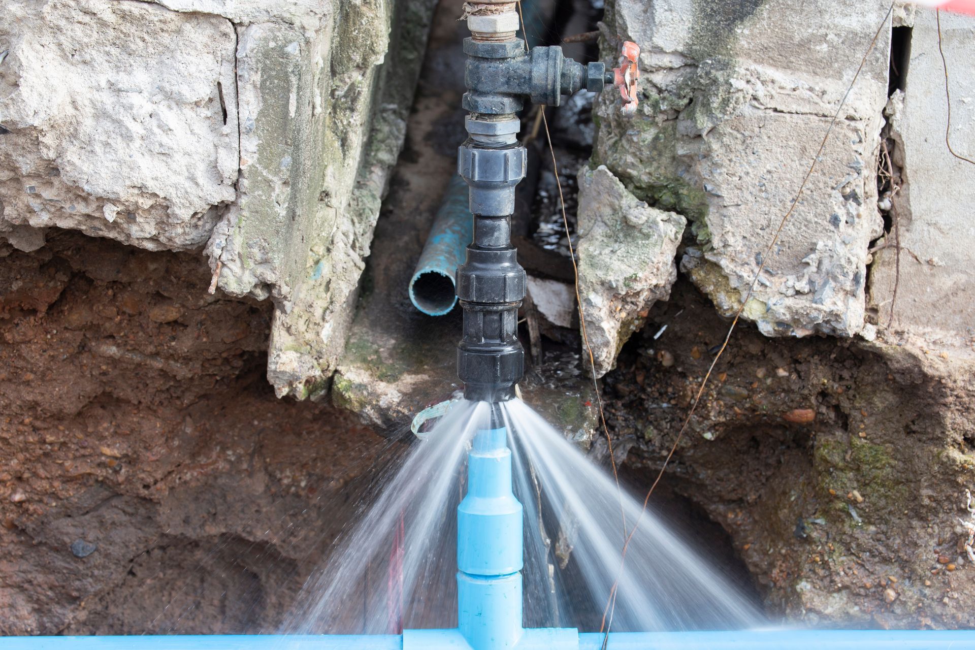 Black pipe spraying water against a rocky wall into a blue trough Black pipe spraying water against a rocky wall into a blue trough