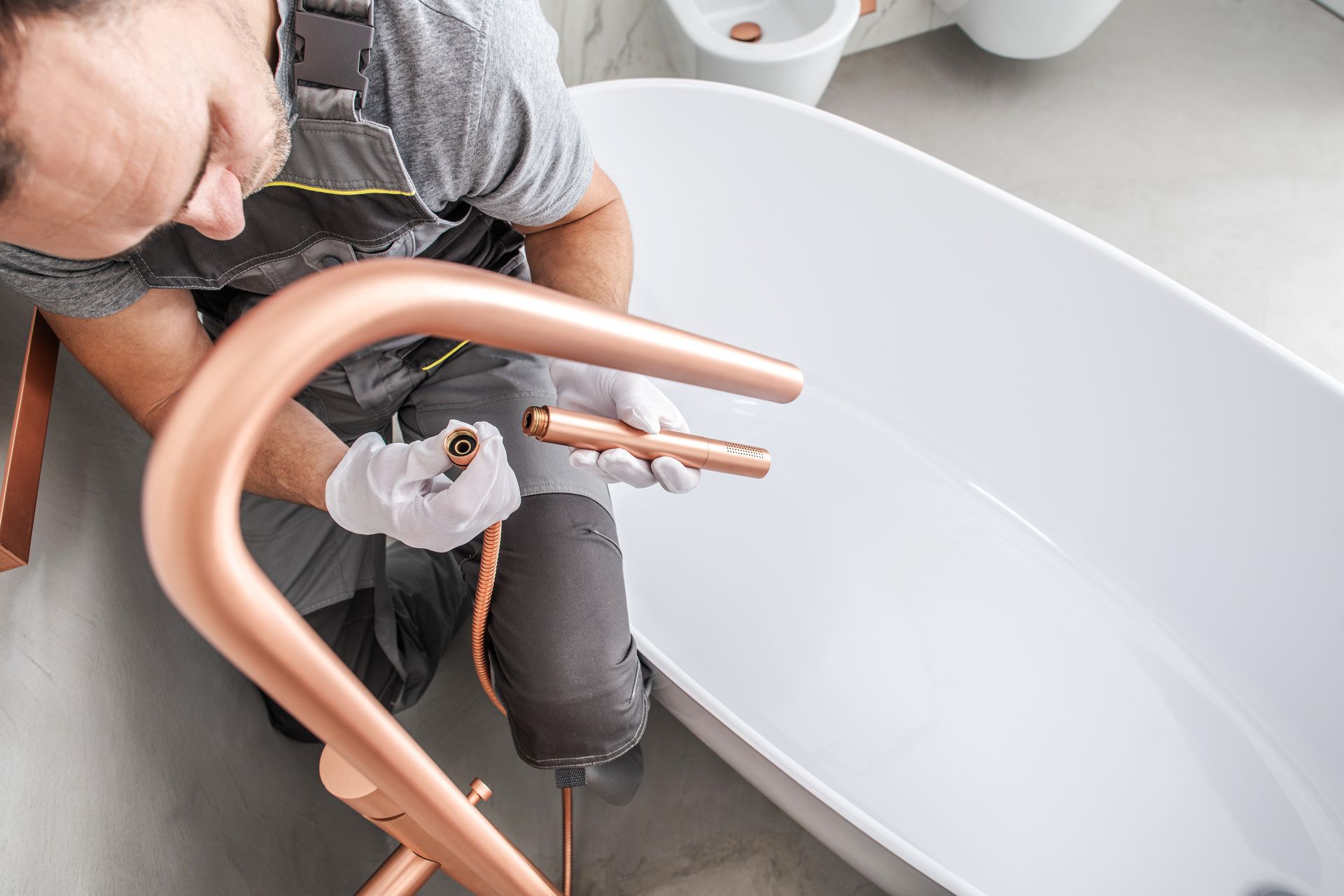 A man is fixing a bathtub, utilising copper pipes and various tools in a residential bathroom.
