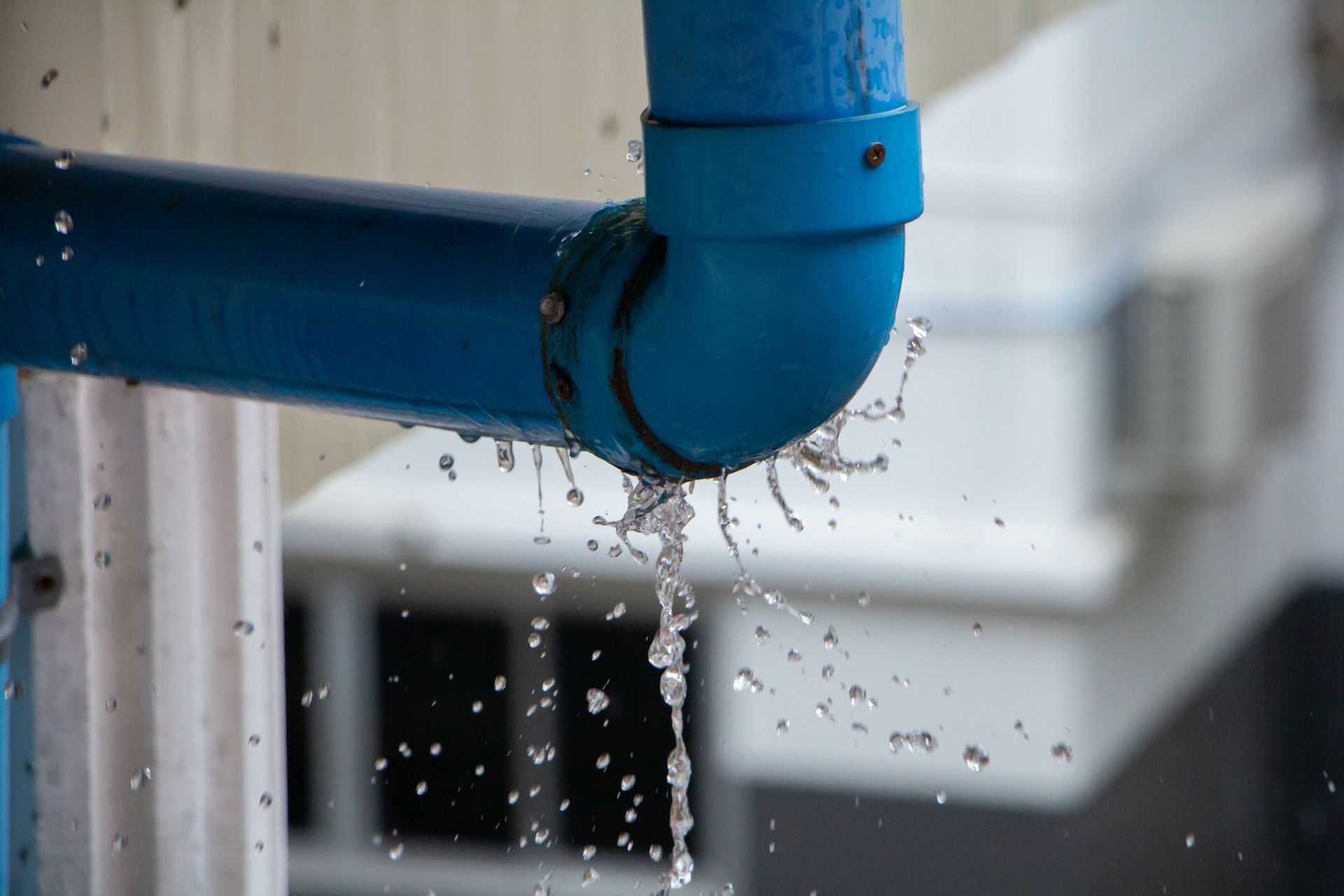 Blue pipe elbow leaking water drops against a blurred industrial background Blue pipe elbow leaking water drops against a blurred industrial background