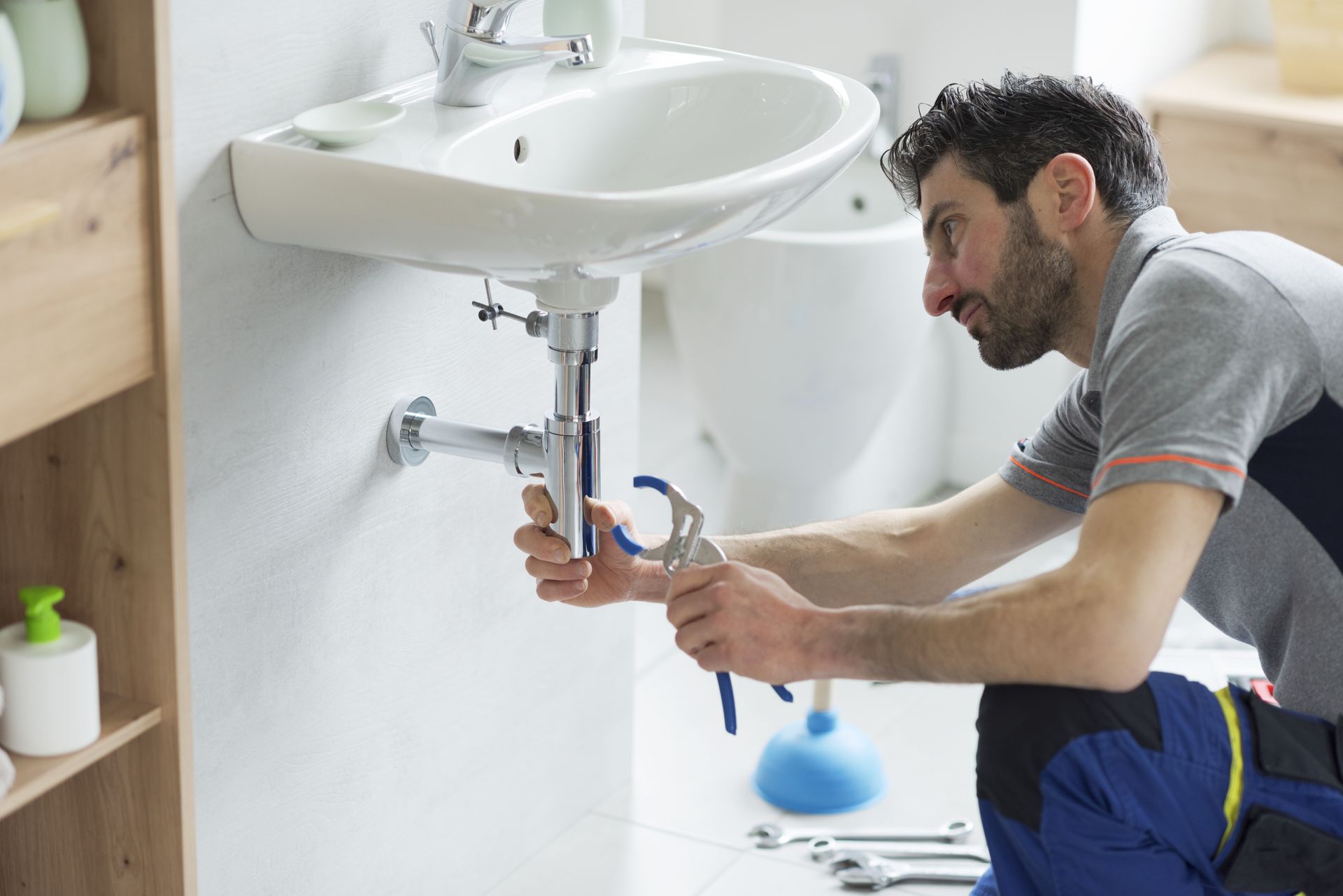 Plumber tightening pipes under a white sink in a bathroom Plumber tightening pipes under a white sink in a bathroom