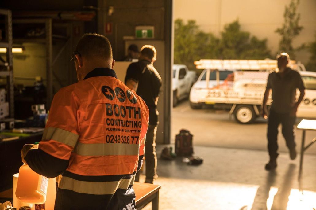 Worker in orange safety vest stands in a garage with another person and a service truck outside. Worker in orange safety vest stands in a garage with another person and a service truck outside.