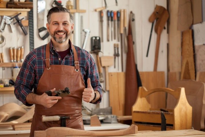 Woodworker in a workshop holding a hand tool, with tools and wooden projects on the workbench.