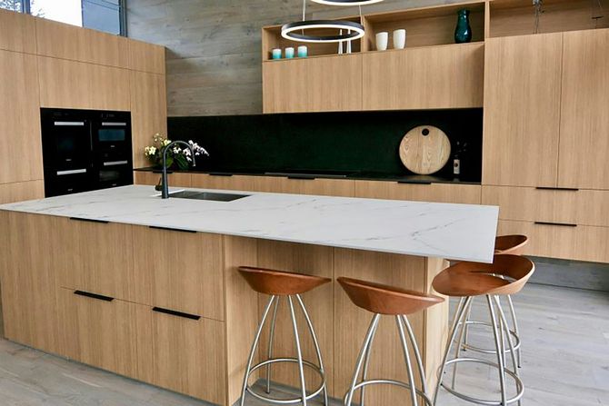 Modern kitchen with wood cabinetry, white island, bar stools, and built-in appliances