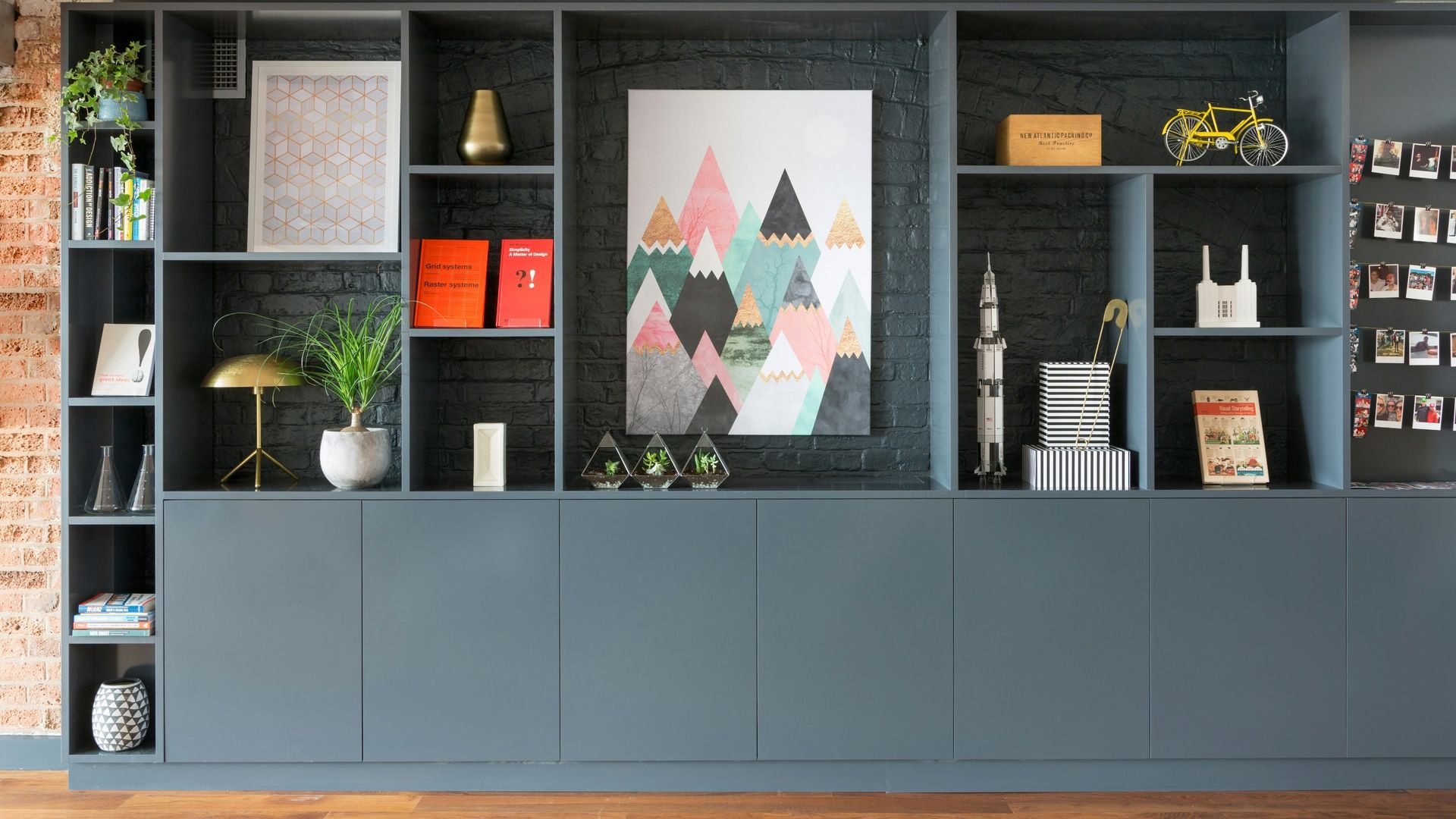Modern wall unit with blue cabinets, open shelves, framed art, books, plants, and decor in a living room