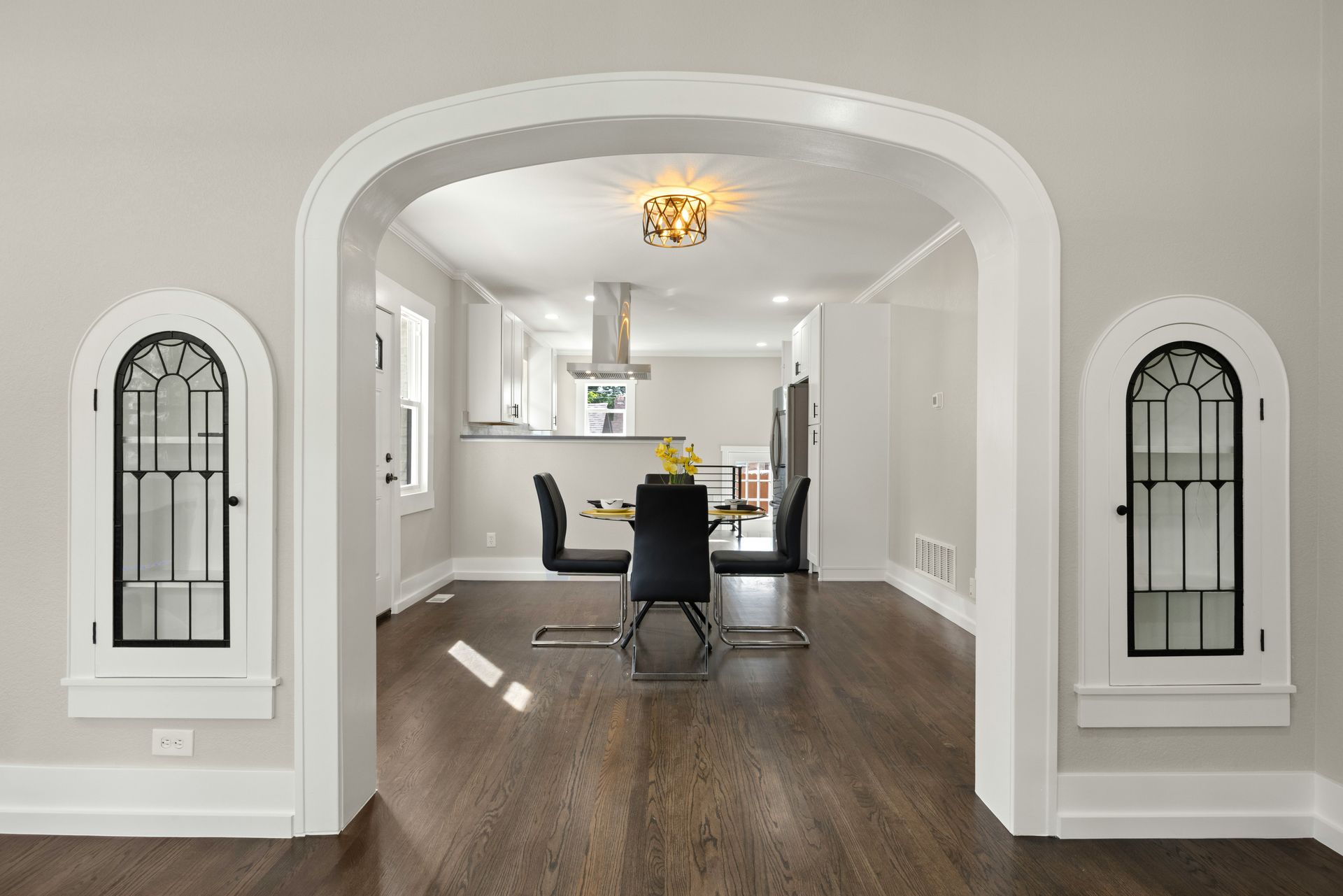 Bright arched doorway into a white dining room with dark wood floors and a table with chairs