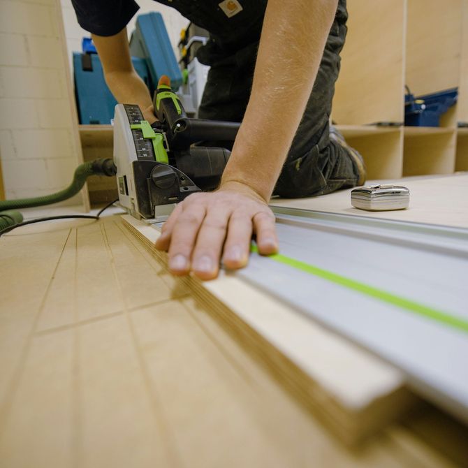 Person using a circular saw to cut a white board on a workbench, with a green guide strip.