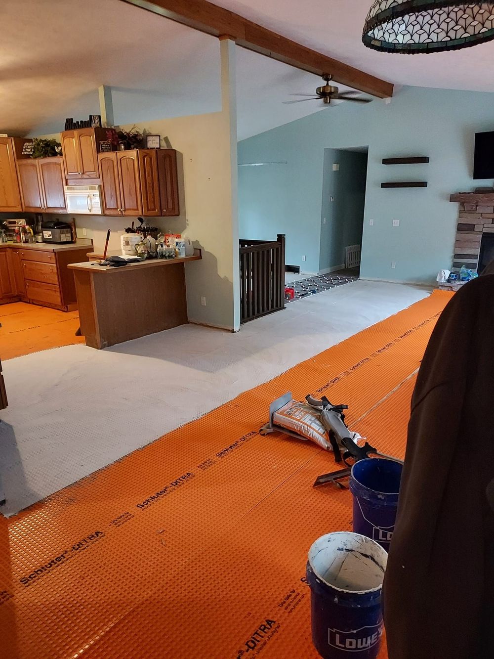 An orange underlayment membrane is installed on a floor, with buckets and construction tools nearby in a house.