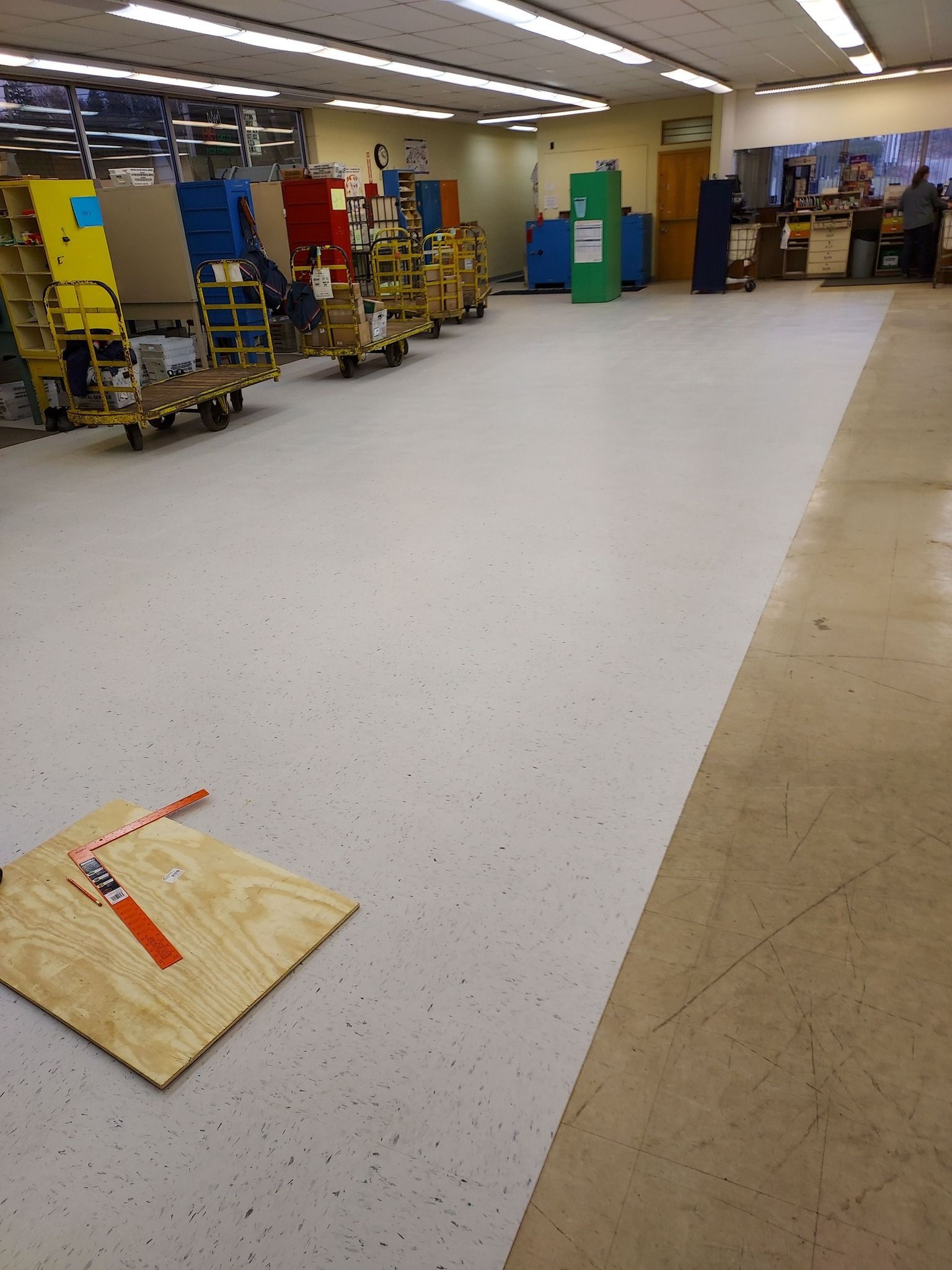 A wide view of a warehouse floor with a newly installed white speckled section next to older flooring and rolling carts.
