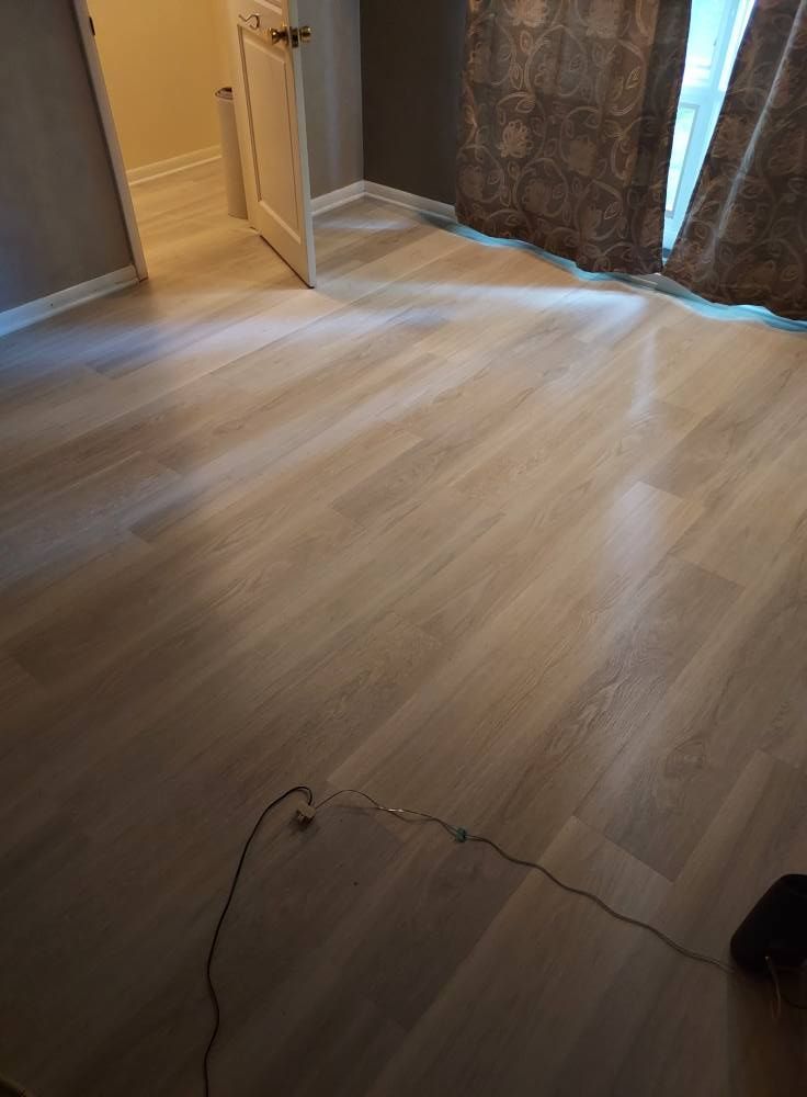 A light-toned wood floor in a room with a partially open white door and long, patterned curtains.