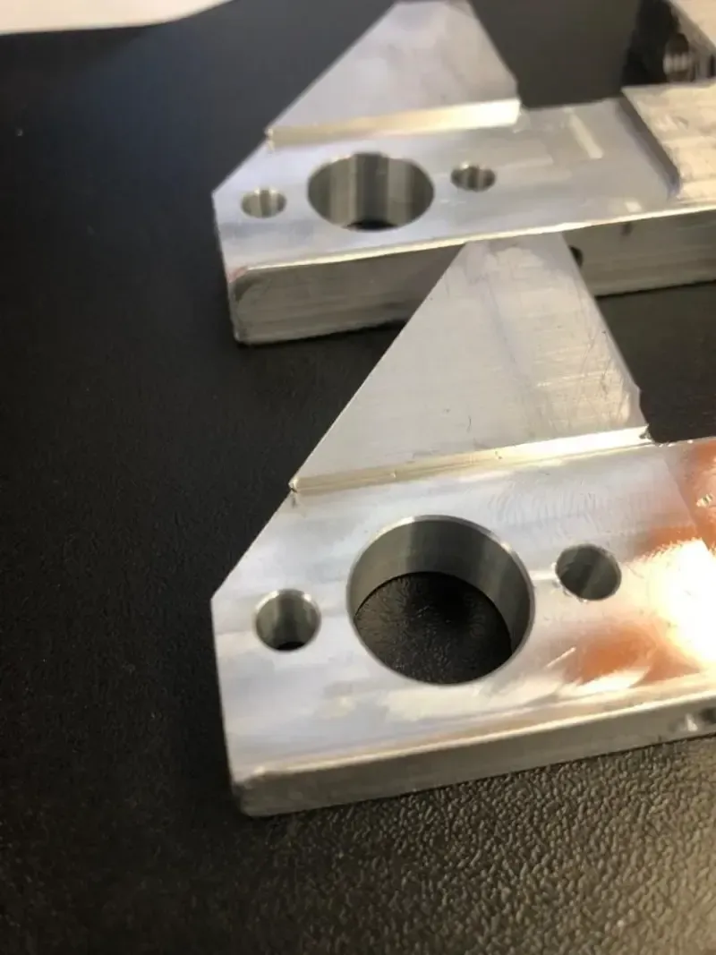 Primo piano di tre parti in alluminio lavorate con estensioni triangolari e fori circolari.