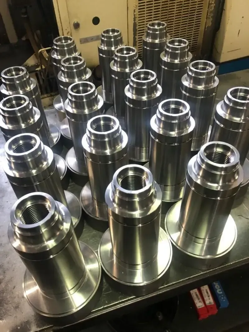 Parti metalliche lavorate con una base e un corpo cilindrico a gradini sono appoggiate su una superficie, probabilmente in un'officina.
