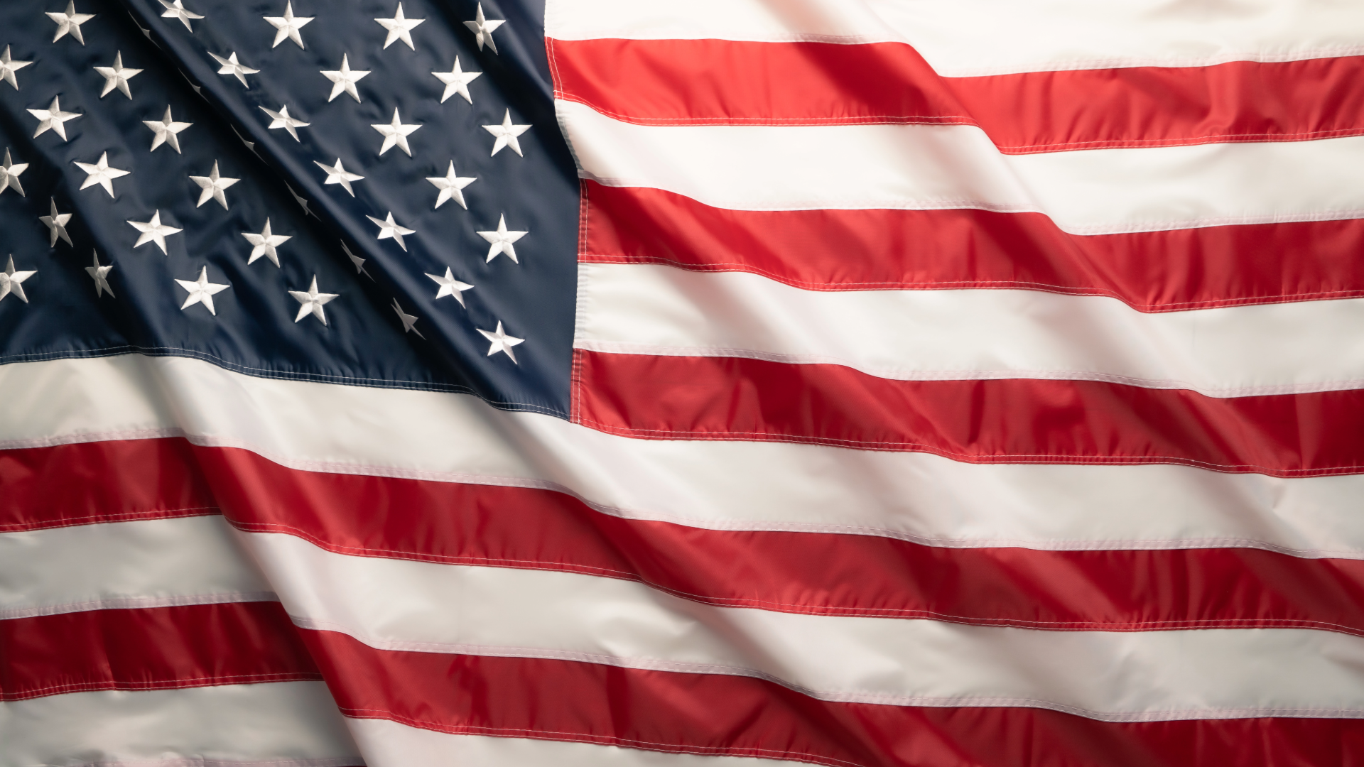 American flag waving in the wind, with red and white stripes and white stars on a blue field