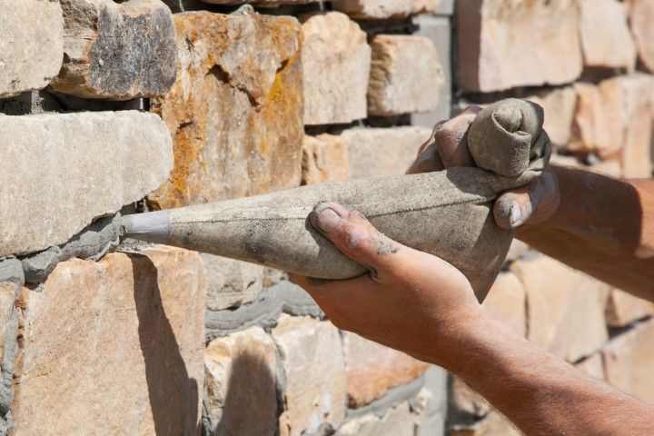 Hands shaping wet mortar against a stacked stone wall during masonry work