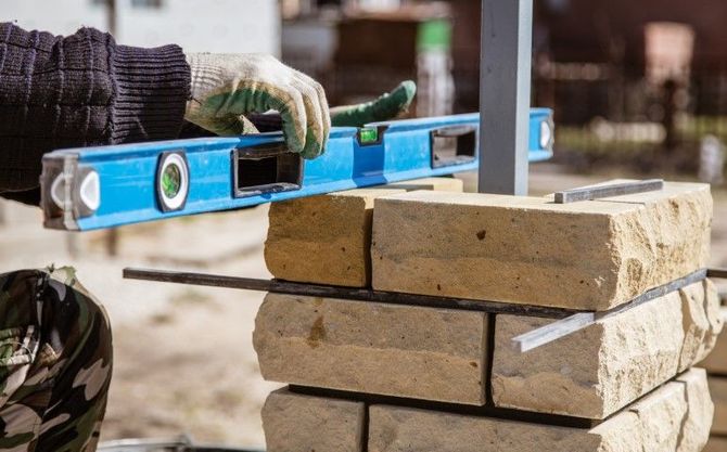 Gloved worker leveling stacked bricks with a blue spirit level outdoors