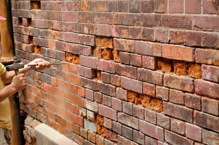 Worker chipping away damaged red brick wall with a hand tool