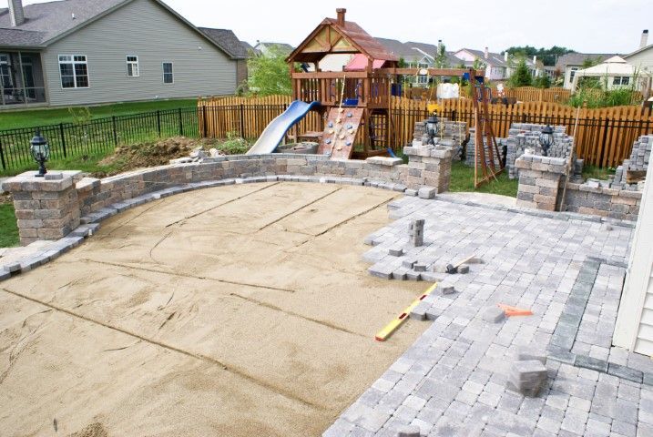 Backyard playset beside a partially paved patio and curved stone retaining wall