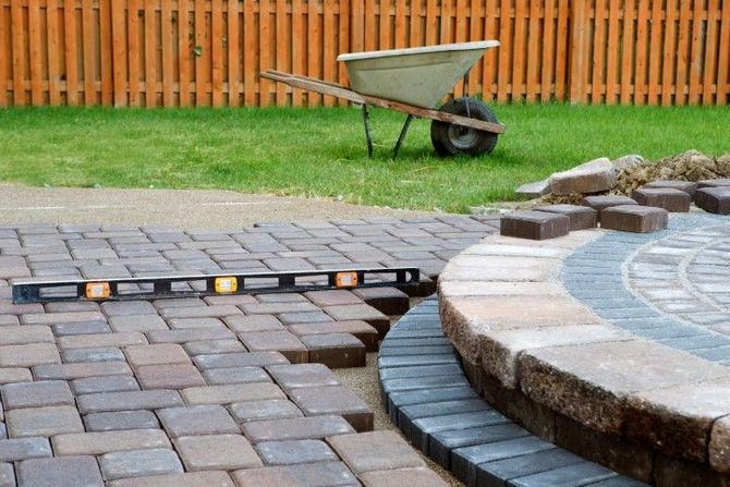 Paver walkway with embedded lights beside a curved stone edge and a wheelbarrow on grass