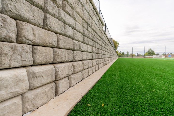 Stone retaining wall beside a green sports field under an overcast sky