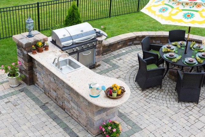 Outdoor stone patio with grill, sink, and round dining table set with dishes and chairs