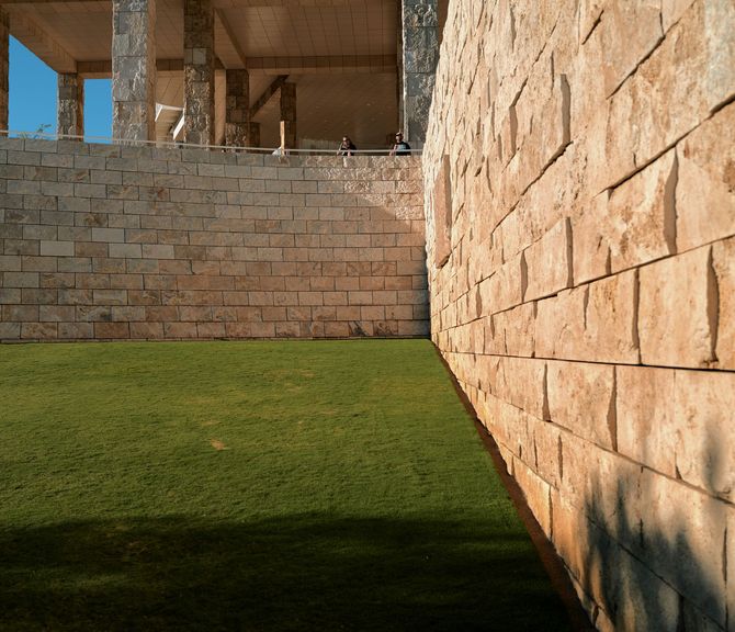 Stone courtyard with green grass, sunlit tan walls, and open pillars in the background
