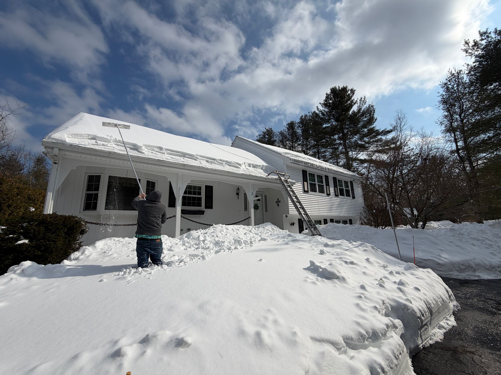 Snow-covered house with a person shoveling the front path under a cloudy winter sky