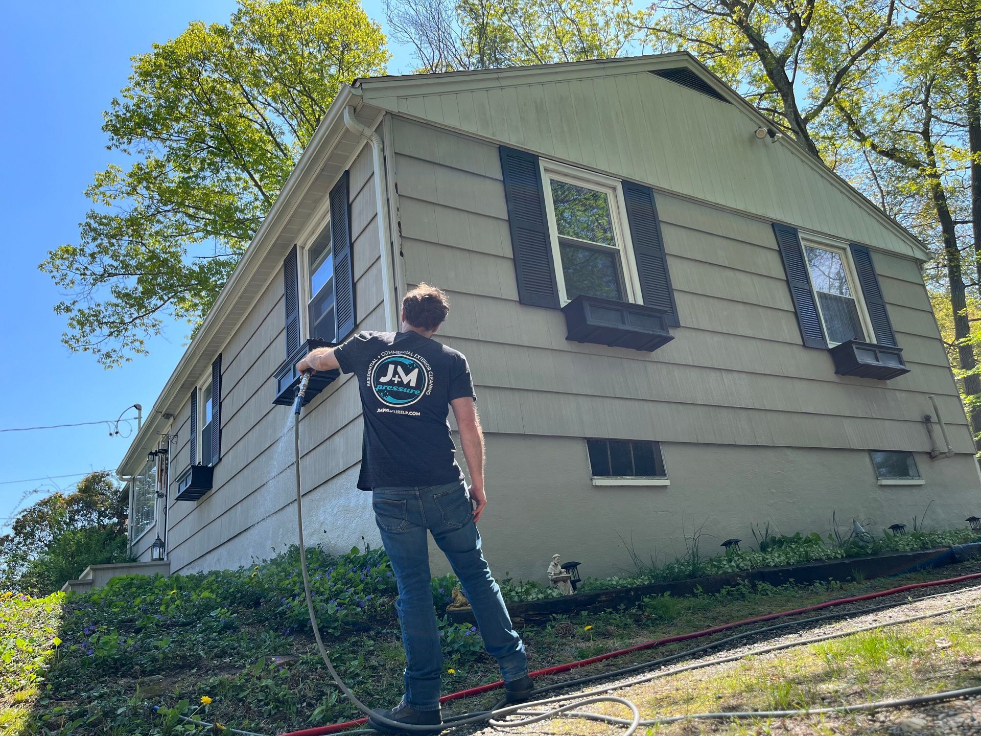 Person stands outside a house, pointing at the roof and window shutters on a sunny day.