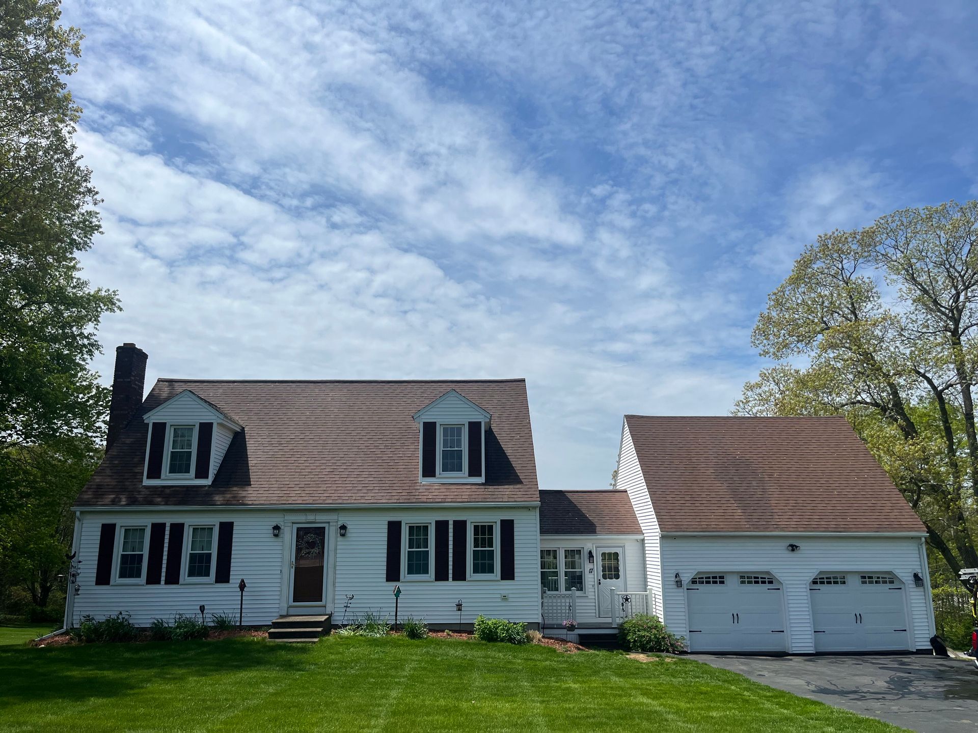 White two-story house with black shutters and attached two-car garage under a blue sky