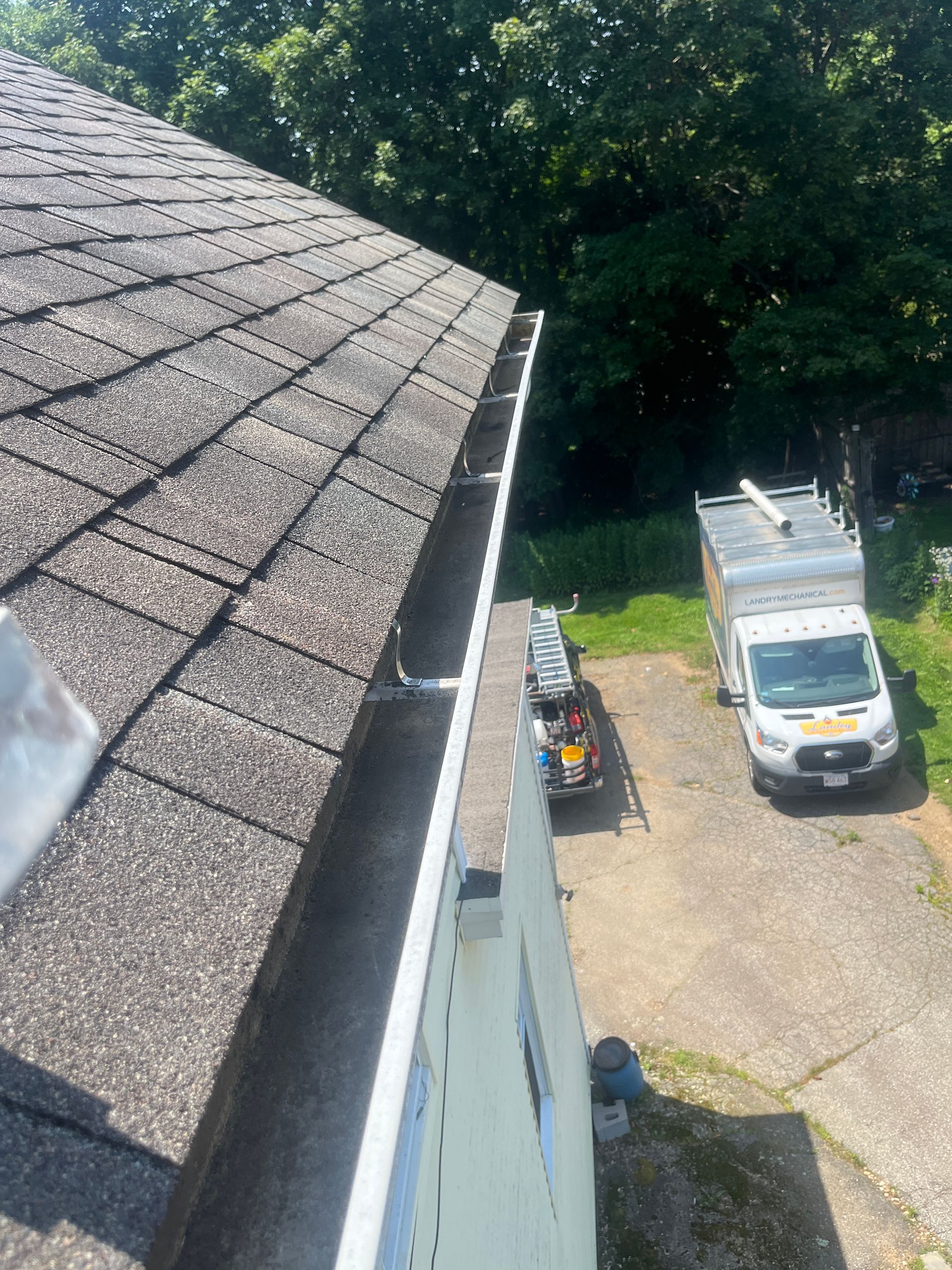 View from a roof edge onto a driveway with a white utility truck and landscaping equipment below