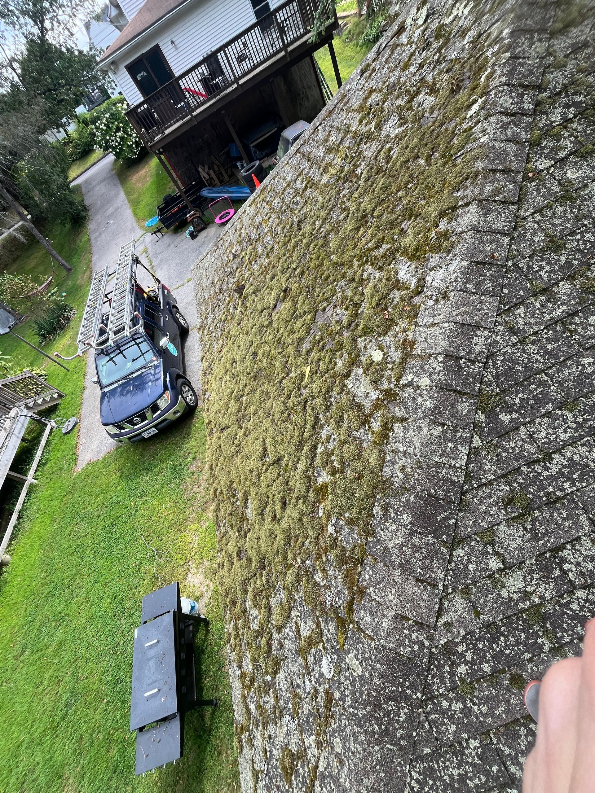 Blue mower on a moss-covered sloped roof beside a house and garden walkway