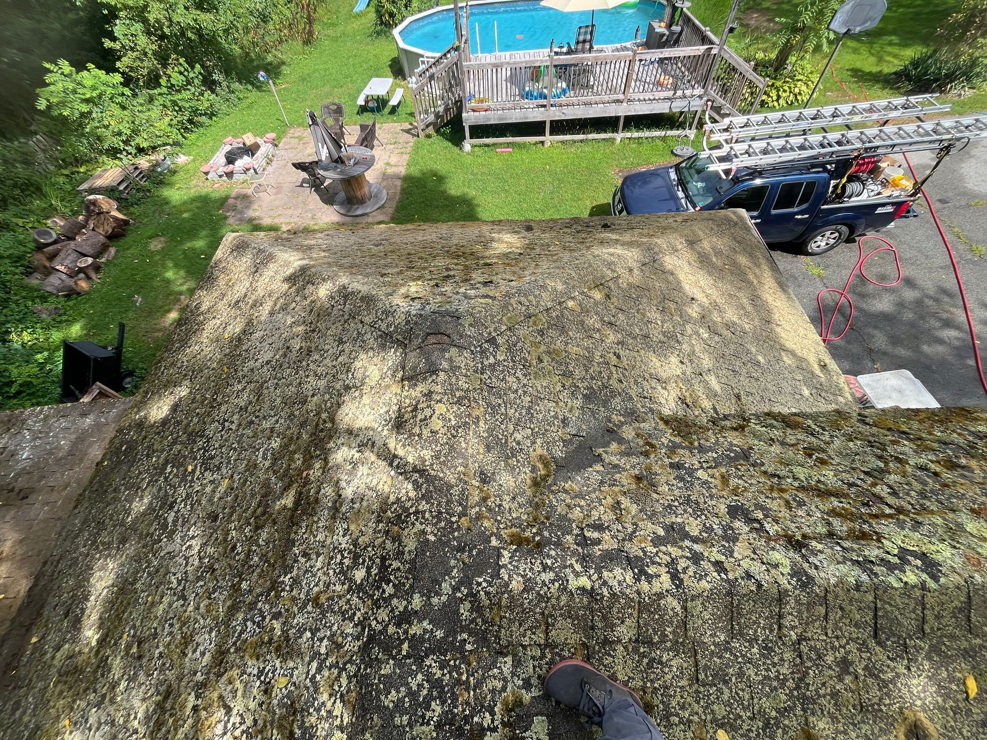 Steep mossy roof seen from above, with a blue pool and a driveway with a truck nearby.
