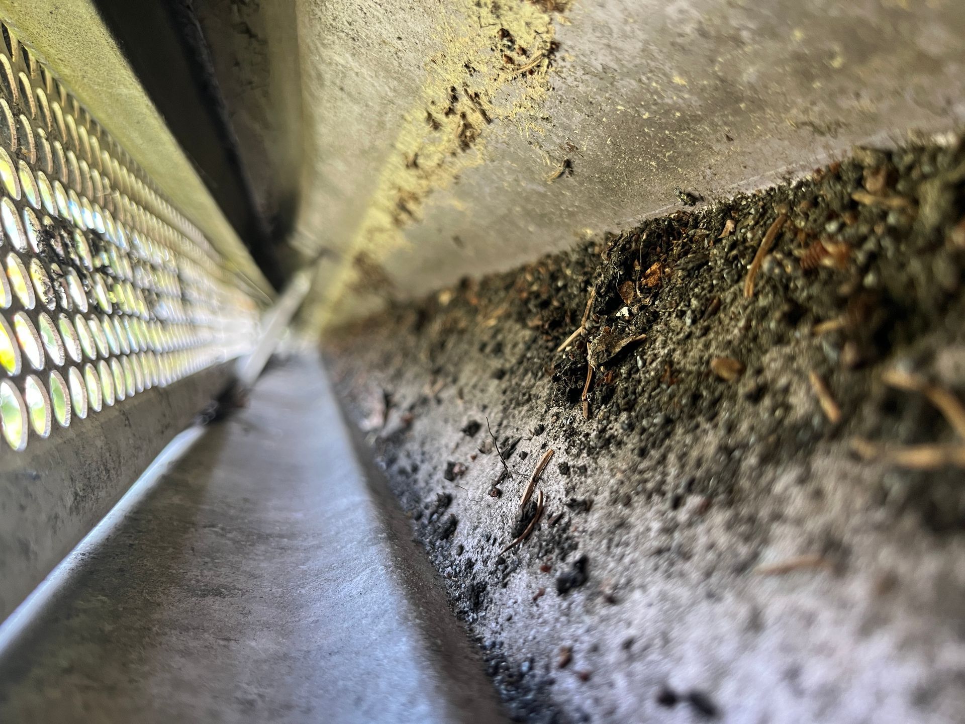 Low-angle view down a narrow concrete corridor beside a perforated metal wall, with rough stained surface on the right