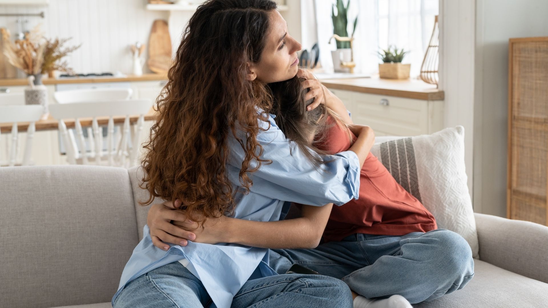 Two people hugging on a gray couch in a bright living room