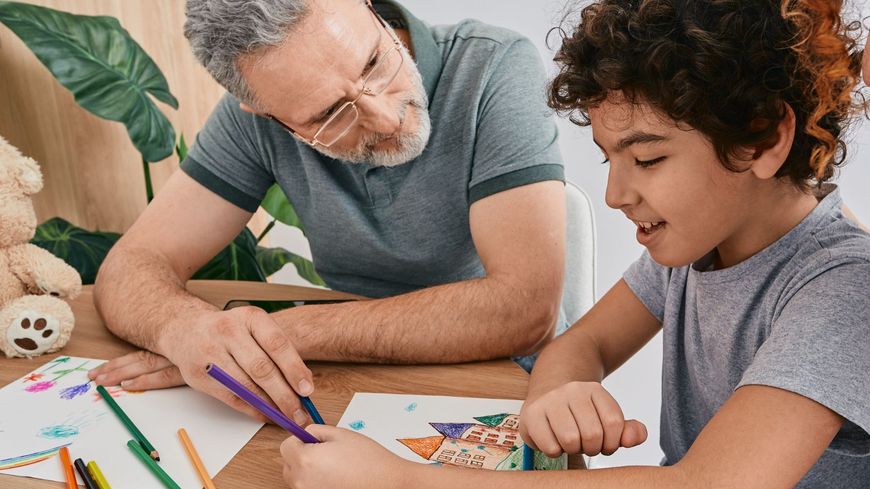 Adult and child drawing together at a table with colored pencils and papers