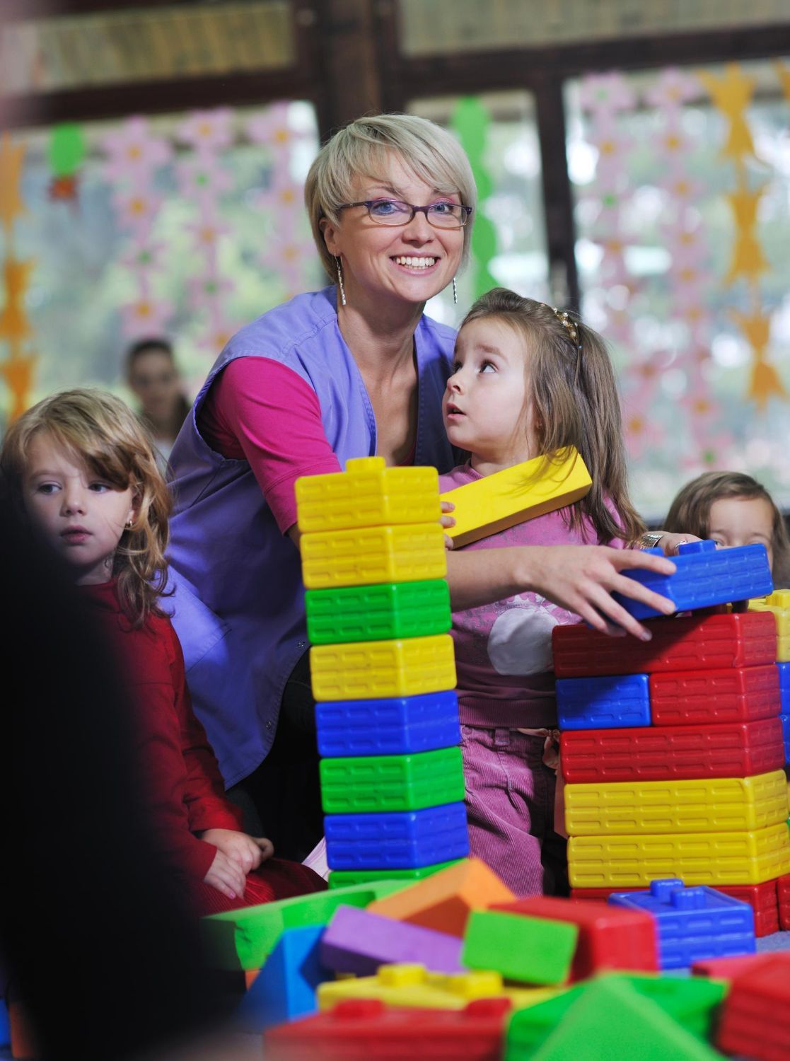 Adult and children building with colorful blocks at a table, one smiling in a classroom-like setting