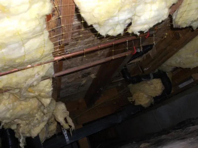 There is a lot of insulation hanging from the ceiling of a house.