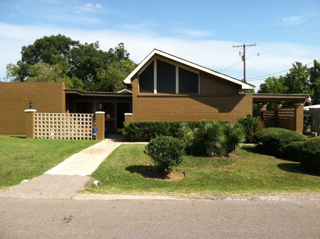 Single-story brick house with a front lawn, sidewalk, and carport under a clear sky