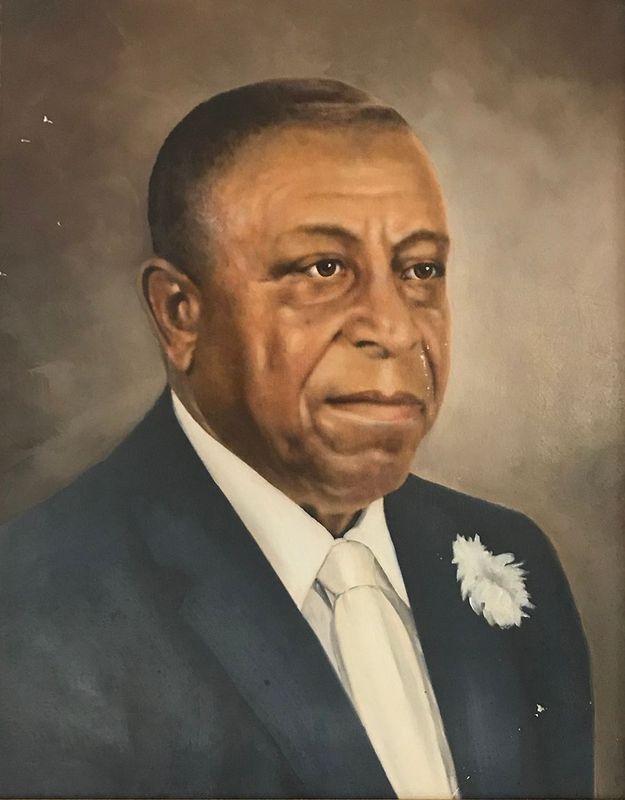 Portrait of a man in a dark suit, white shirt, and tie with a white flower boutonniere on his lapel