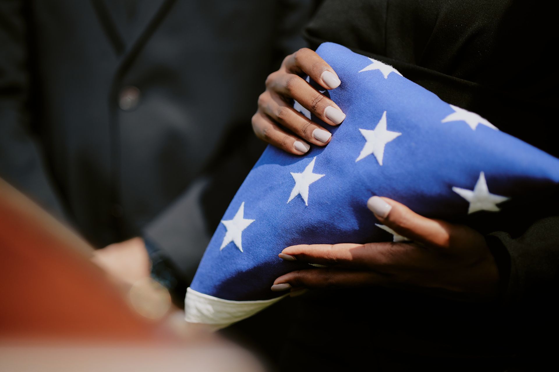 A man in a military uniform is holding an american flag in his hands.