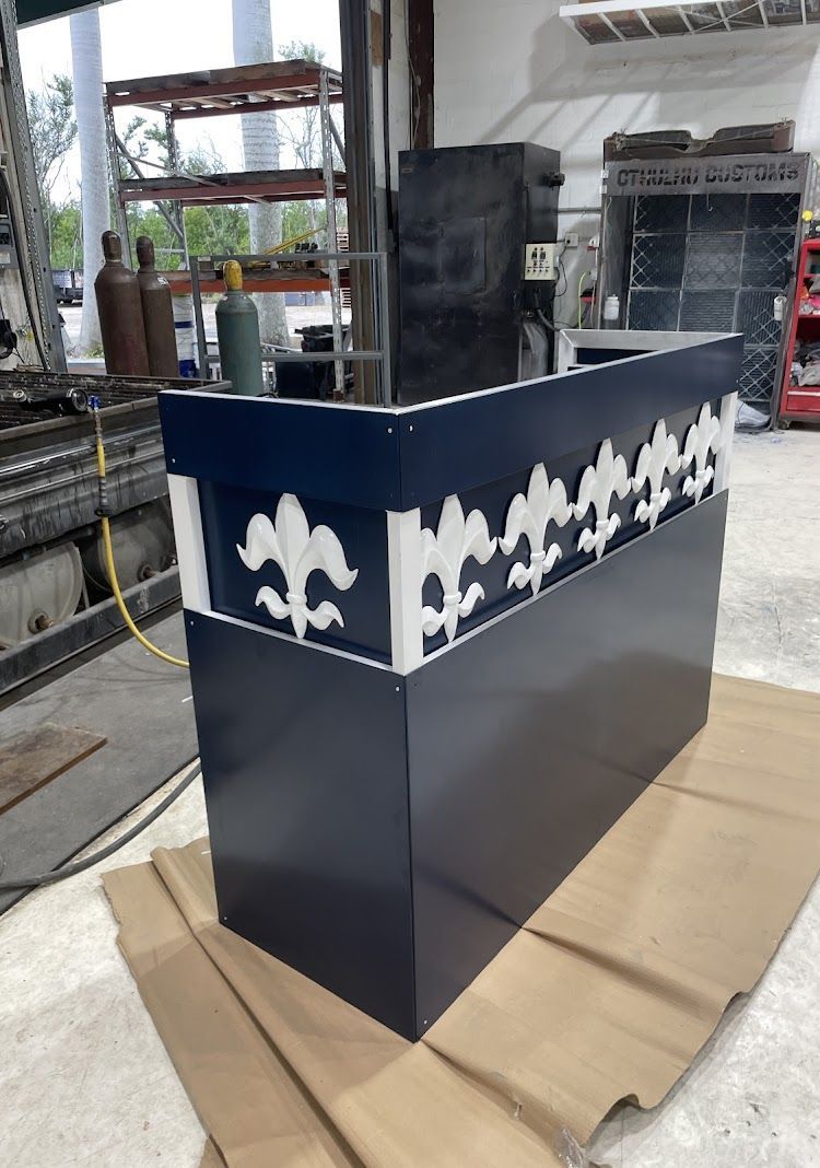 A blue and white metal reception desk with fleur-de-lis design, in a workshop setting.