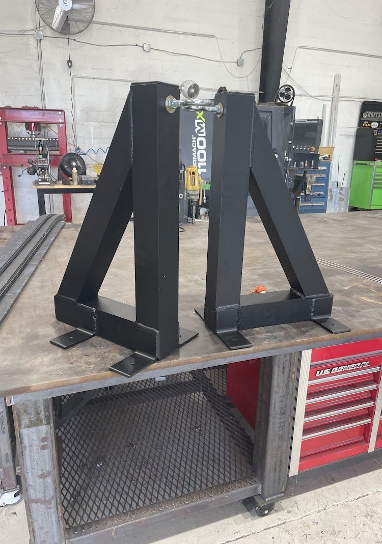 Two black metal A-frame structures, likely for supporting something, sit on a metal workbench in a workshop.