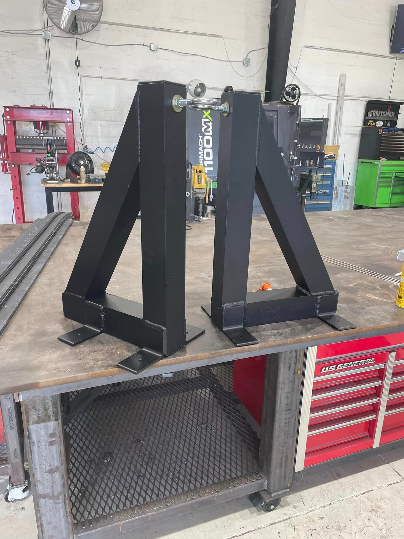 Two black metal fabrication stands on a workbench, ready for assembly.